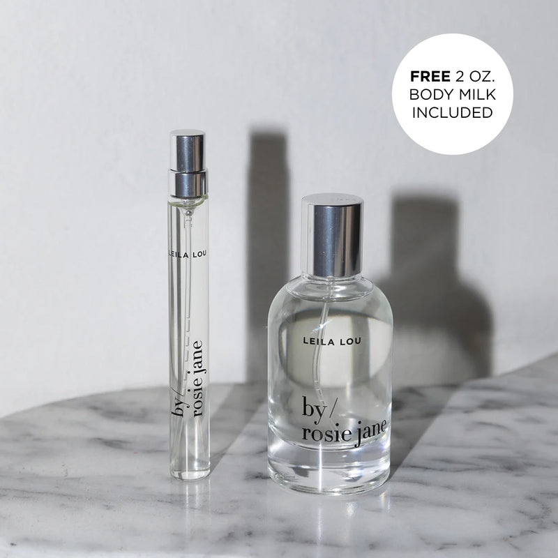 Two Leila Lou perfume bottles on a marble surface with a free body milk offer label.