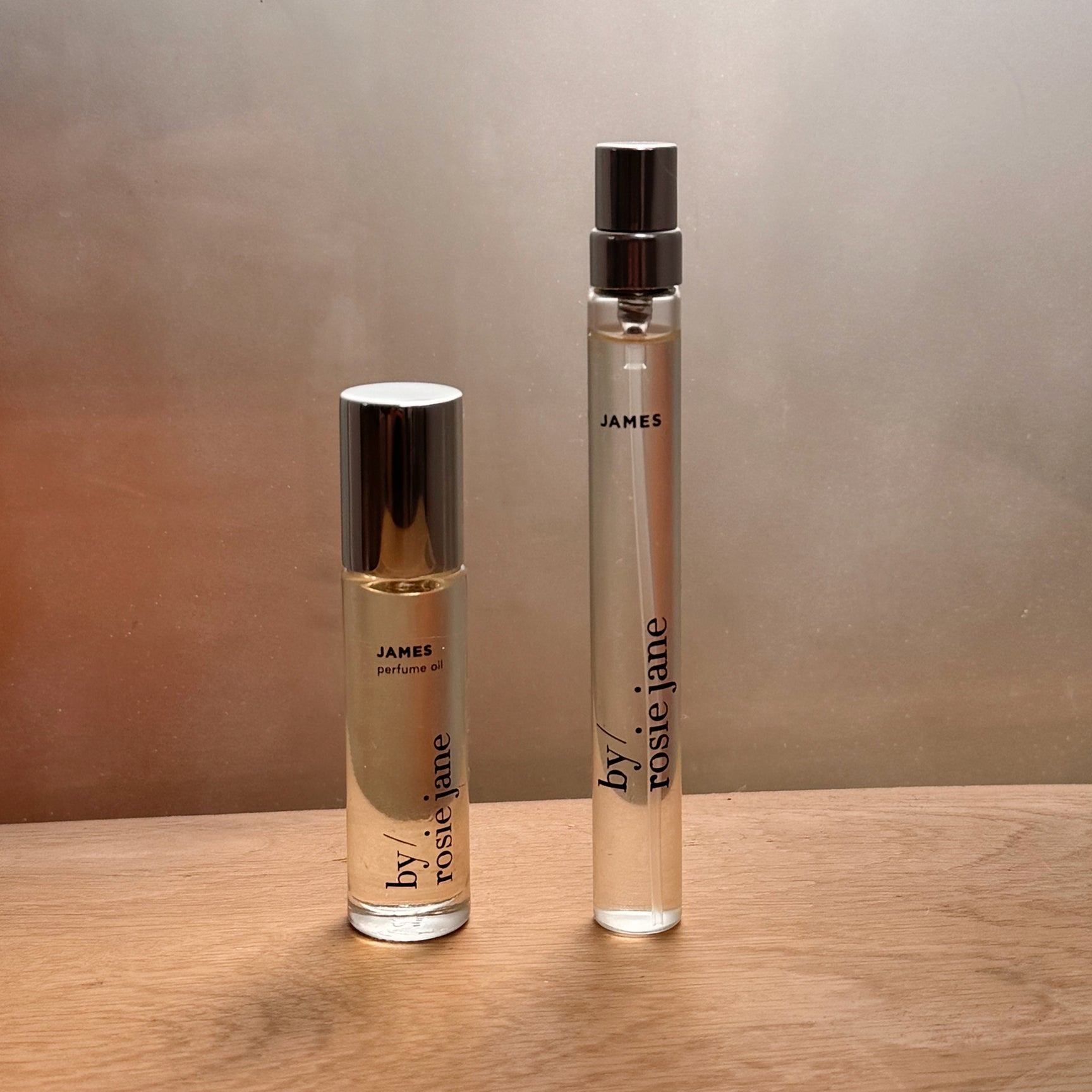 The byrosiejane JAMES 2 WAYS TRAVEL SET, featuring a Perfume Oil and a Travel Spray Eau de Parfum, rests on a wooden surface with soft, neutral lighting—ideal for anyone seeking the perfect summer fragrance.