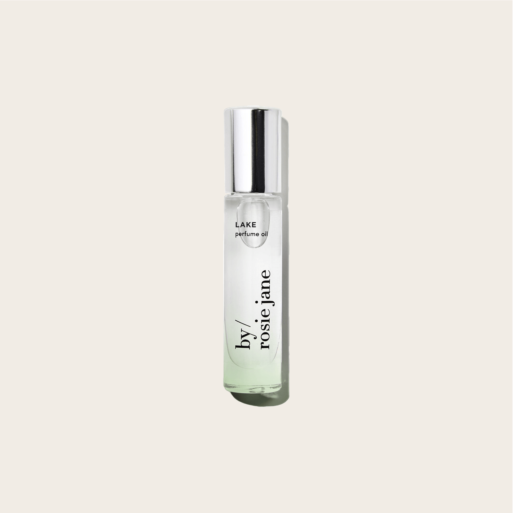 A clear glass perfume bottle with a silver cap, labeled byrosiejane LAKE PERFUME OIL, sits on a light beige background, evoking Lake Tahoe’s calm essence with soft notes of vanilla.