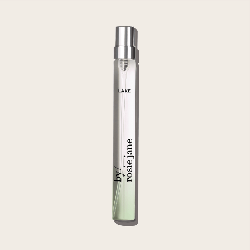 The LAKE TRAVEL SPRAY by byrosiejane is a clear glass perfume vial with a silver cap, featuring neroli and vanilla sandalwood notes inspired by Lake Tahoe.