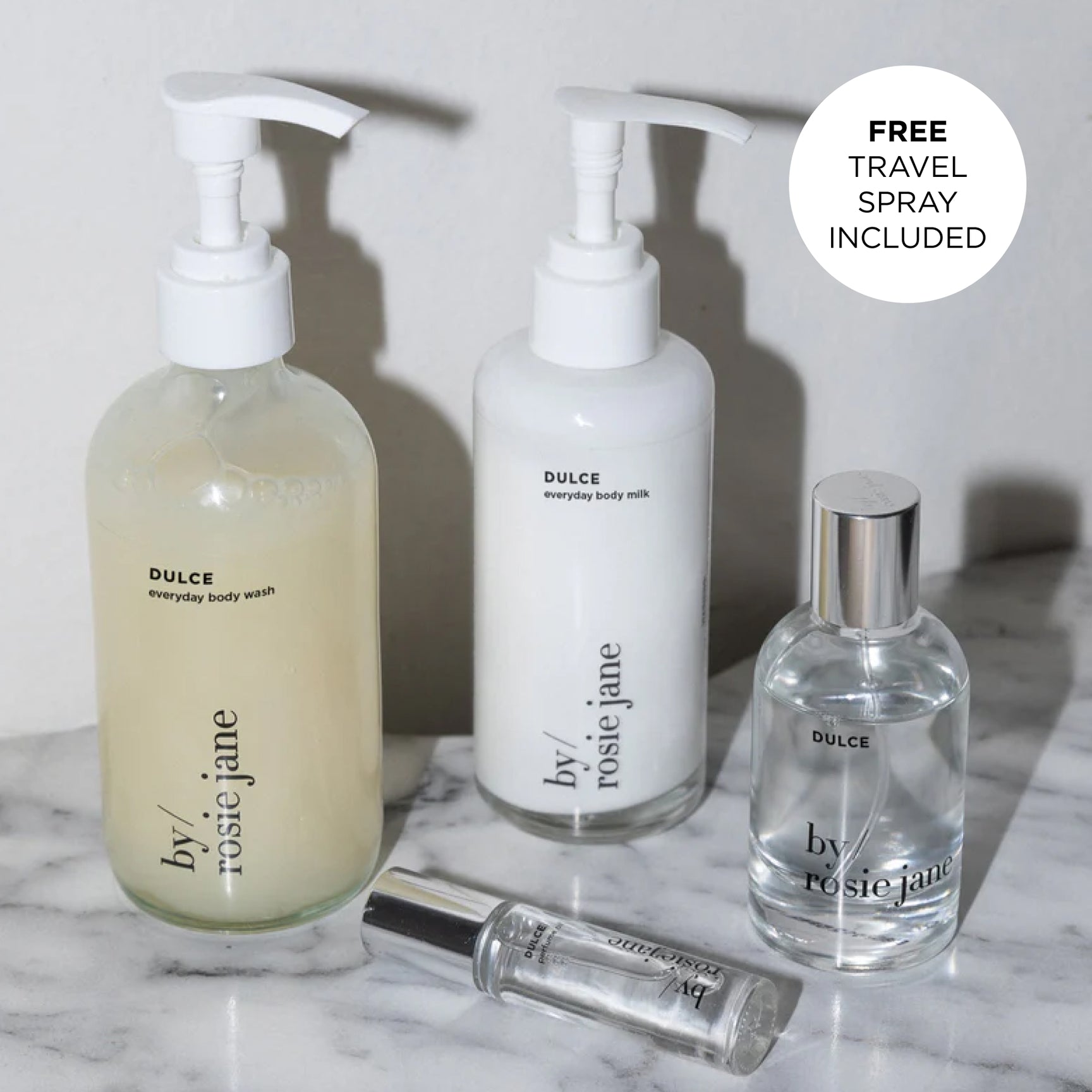 Three bottles of 'by rosie jane' products on a marble surface with a free travel spray included label.