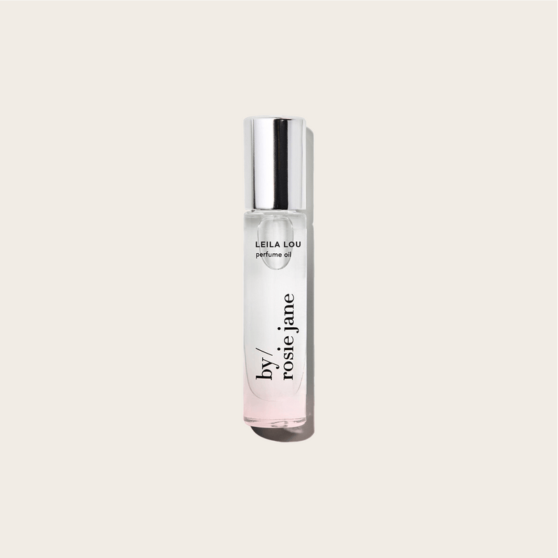The LEILA LOU PERFUME OIL by byrosiejane sits in a clear glass bottle with a silver cap on a light beige background. Its slightly tinted oil offers an ideal everyday scent, perfectly capturing the fresh essence of spring.