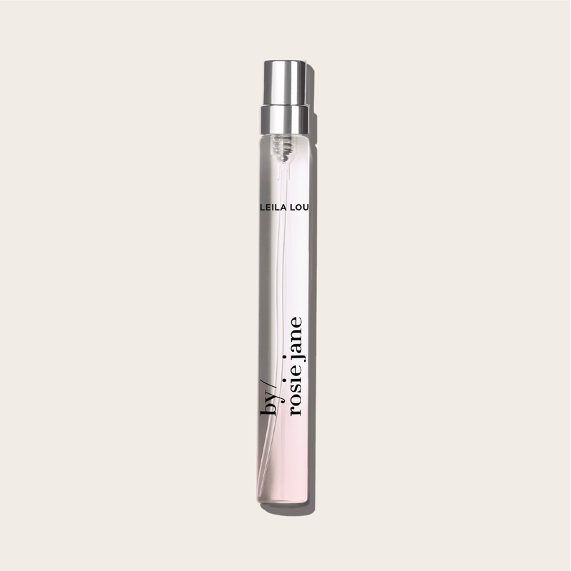 The LEILA LOU TRAVEL SPRAY by byrosiejane stands upright on a light beige background, its clear glass bottle with a silver cap labeled in black, evoking fresh cut grass and delicate jasmine.