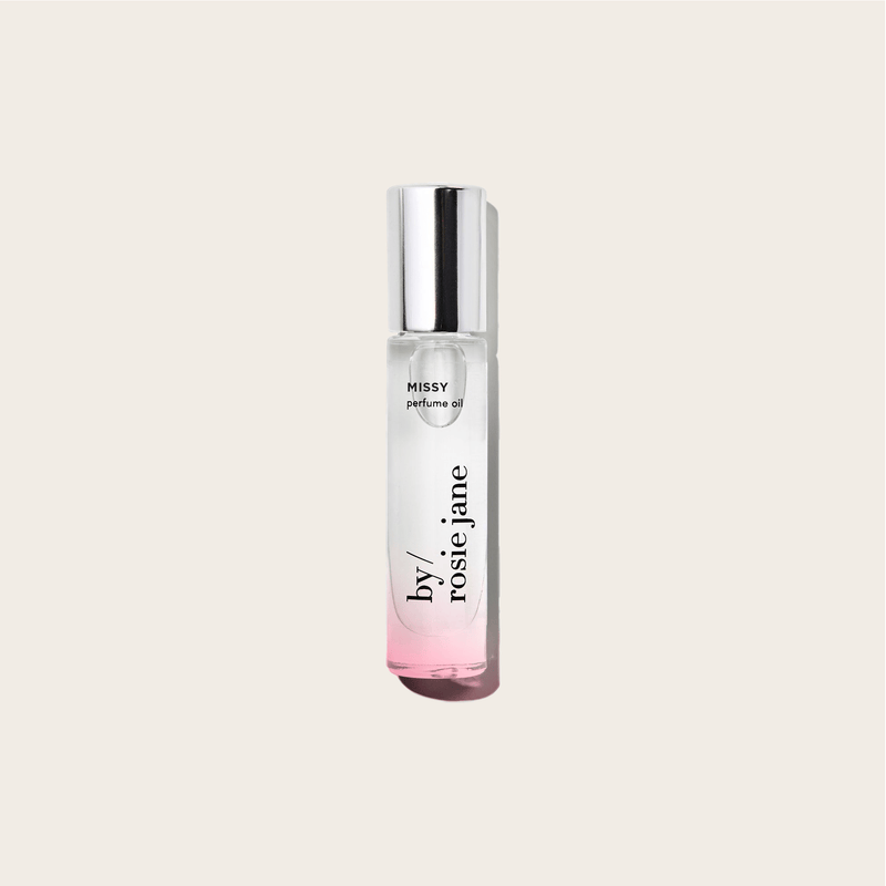 A clear glass bottle of byrosiejane MISSY PERFUME OIL with a shiny silver cap and a pink gradient base, set against a light beige background—featuring refreshing green mandarin notes.