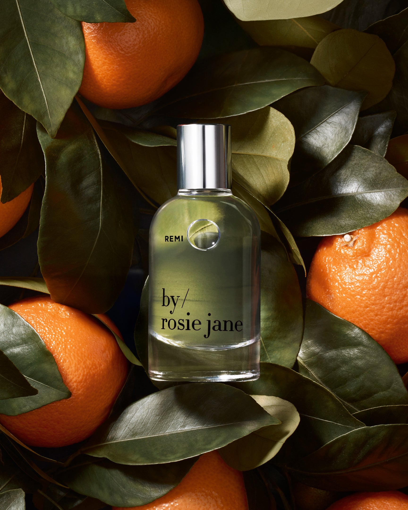Remi Perfume bottle labeled 'by rosie jane' surrounded by oranges and leaves