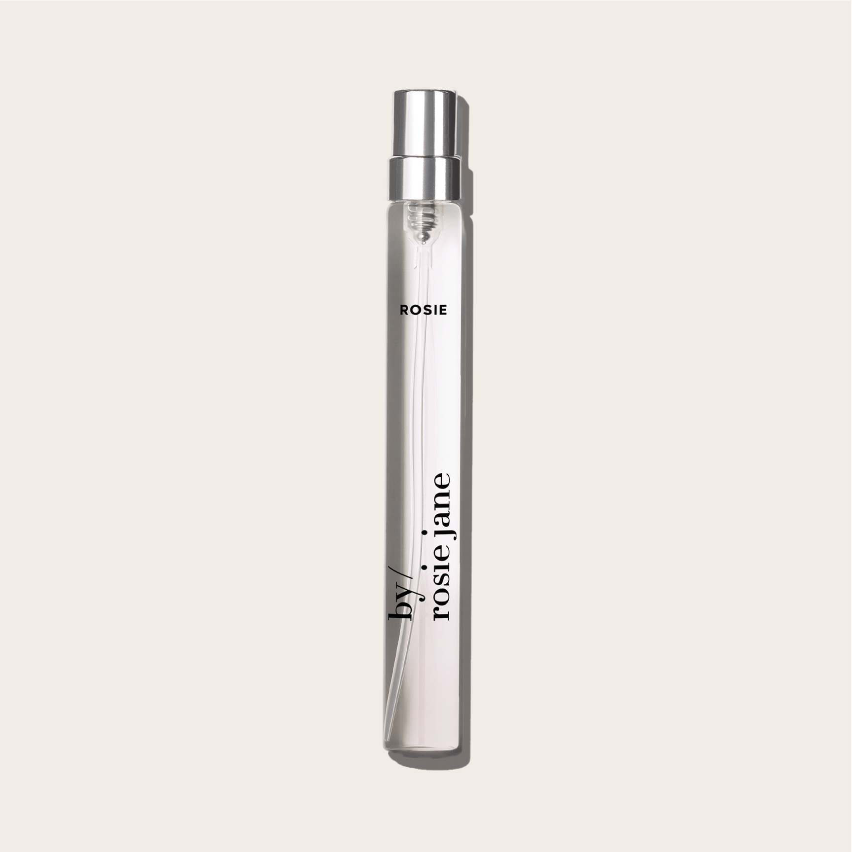 A clear glass perfume spray bottle labeled byrosiejane with ROSIE TRAVEL SPRAY near the top, featuring notes of nude musk, set against a light beige background.