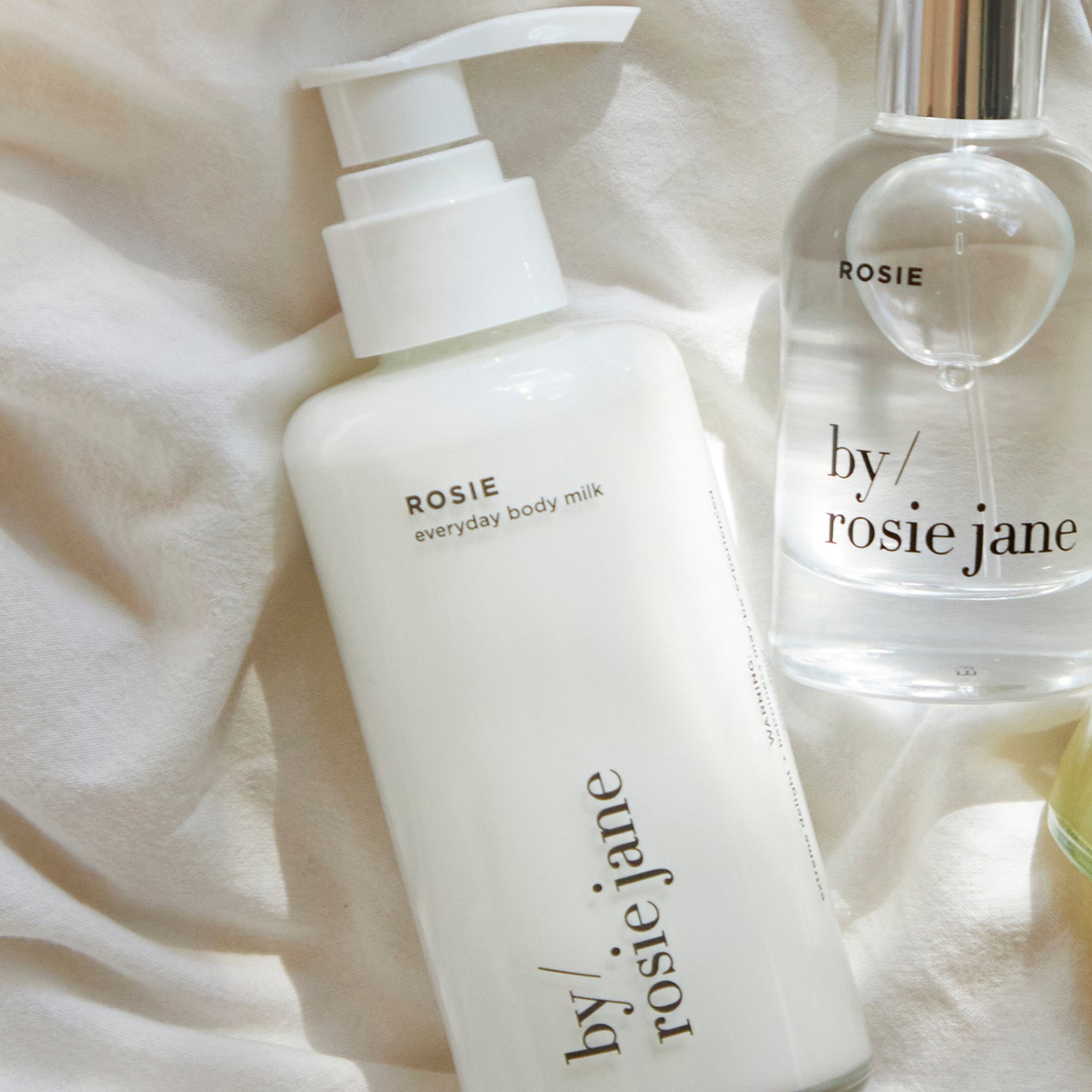 The YOU SMELL GOOD DUO by byrosiejane, featuring everyday body milk and eau de parfum in clear, elegantly labeled bottles, is placed on a white fabric surface.