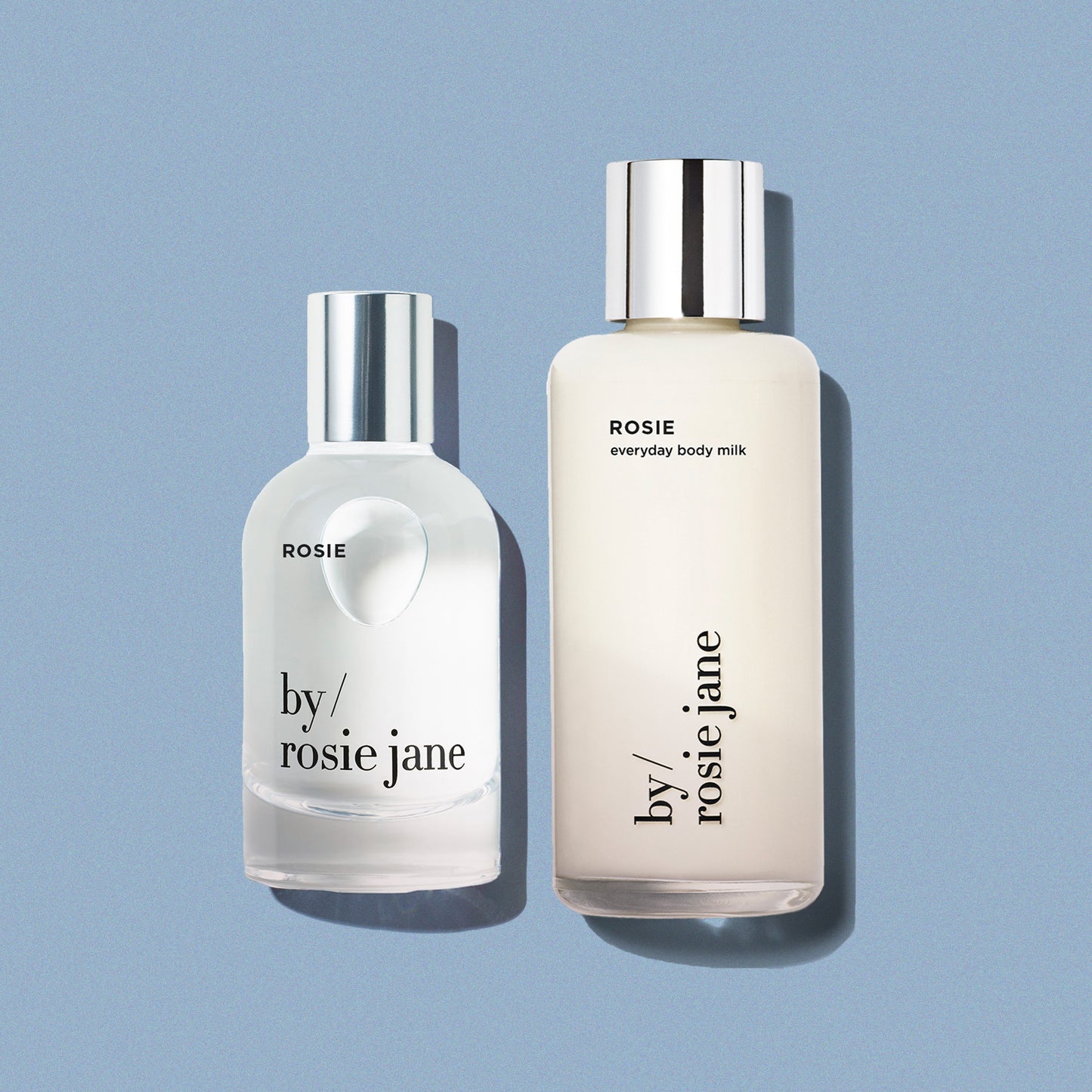 Two bottles of 'by rosie jane' products on a light blue background- body milk and perfume