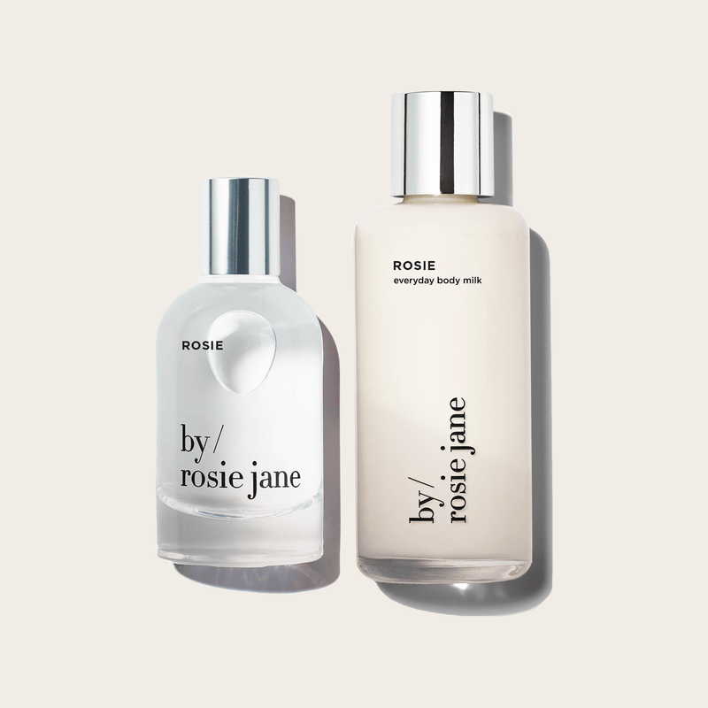 The ROSIE YOU SMELL GOOD DUO by byrosiejane features two clear bottles with silver caps on a beige background—ROSIE eau de parfum and everyday body milk—both offering an effortlessly soft, modern nude musk scent.