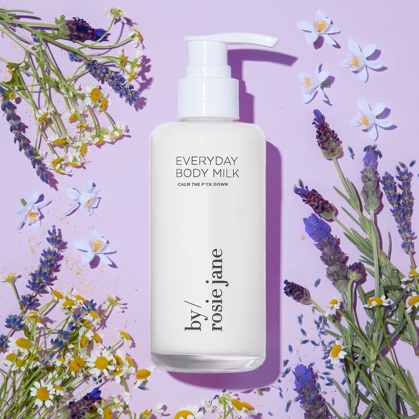 Calm The F*ck Down Everyday Body Milk bottle surrounded by flowers, offering hydration, anti-aging benefits, and soothing properties with organic turmeric and aloe vera.