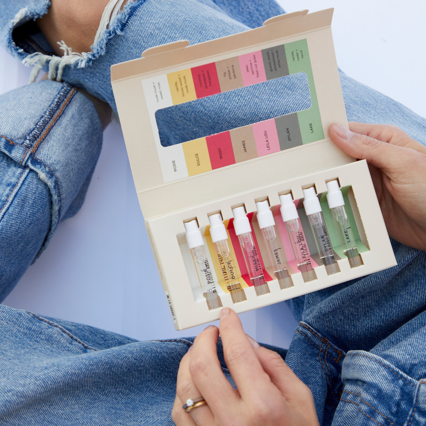 Person holding the Fragrance Discovery Set box featuring seven small bottles of clean perfumes, including scents like vanilla, jasmine, and sandalwood.