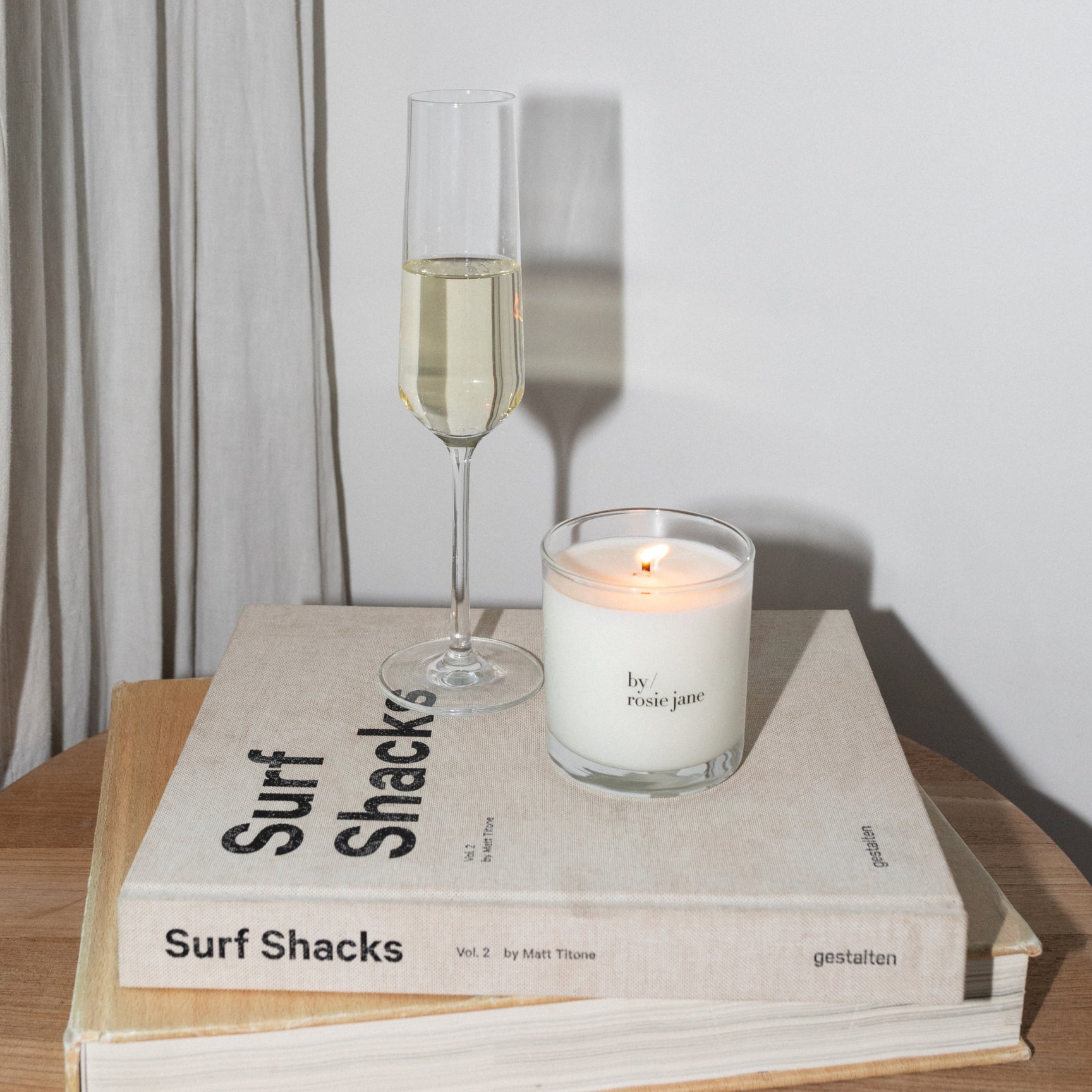 Glass of champagne and candle on a book with the 'by rosie jane' candle lit 
