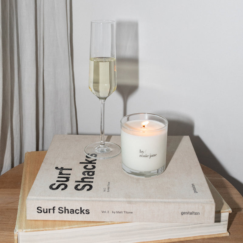 Glass of champagne and candle on a book with the 'by rosie jane' candle lit 