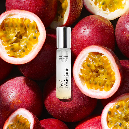 Perfume oil bottle labeled matilda 'Rosie Jane' surrounded by halved passion fruits