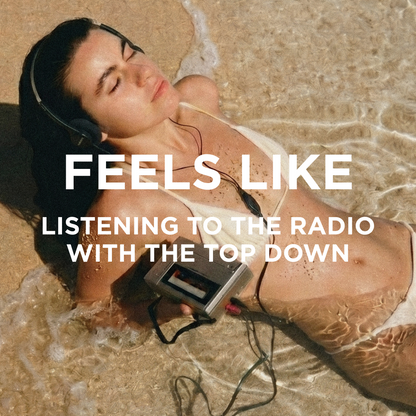 A woman lying on a sandy beach in shallow water, wearing over-ear headphones and holding a cassette tape player. Large white text across the center reads, 'FEELS LIKE LISTENING TO THE RADIO WITH THE TOP DOWN.