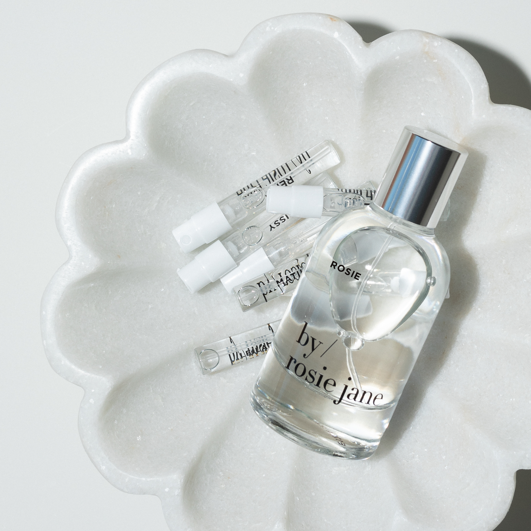 Perfume bottle labeled 'by rosie jane' on a white marble surface