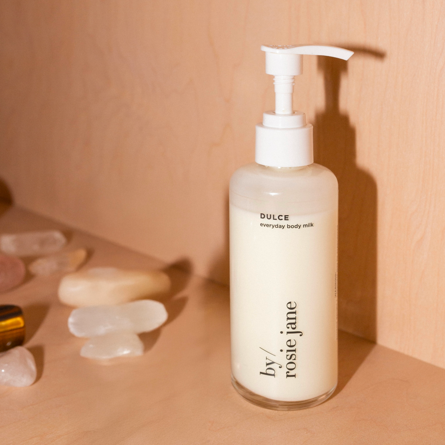 Bottle of 'Dulce' body milk by 'rosie jane' on a beige background with crystals.