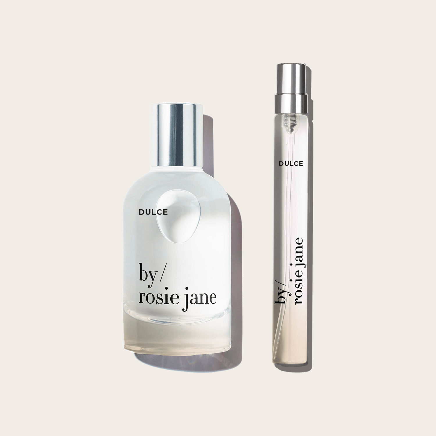 The DULCE HOME + AWAY SET byrosiejane includes two clear glass bottles with warm vanilla notes: a large eau de parfum with a silver cap and a slim travel spray, both displayed on a light beige background.