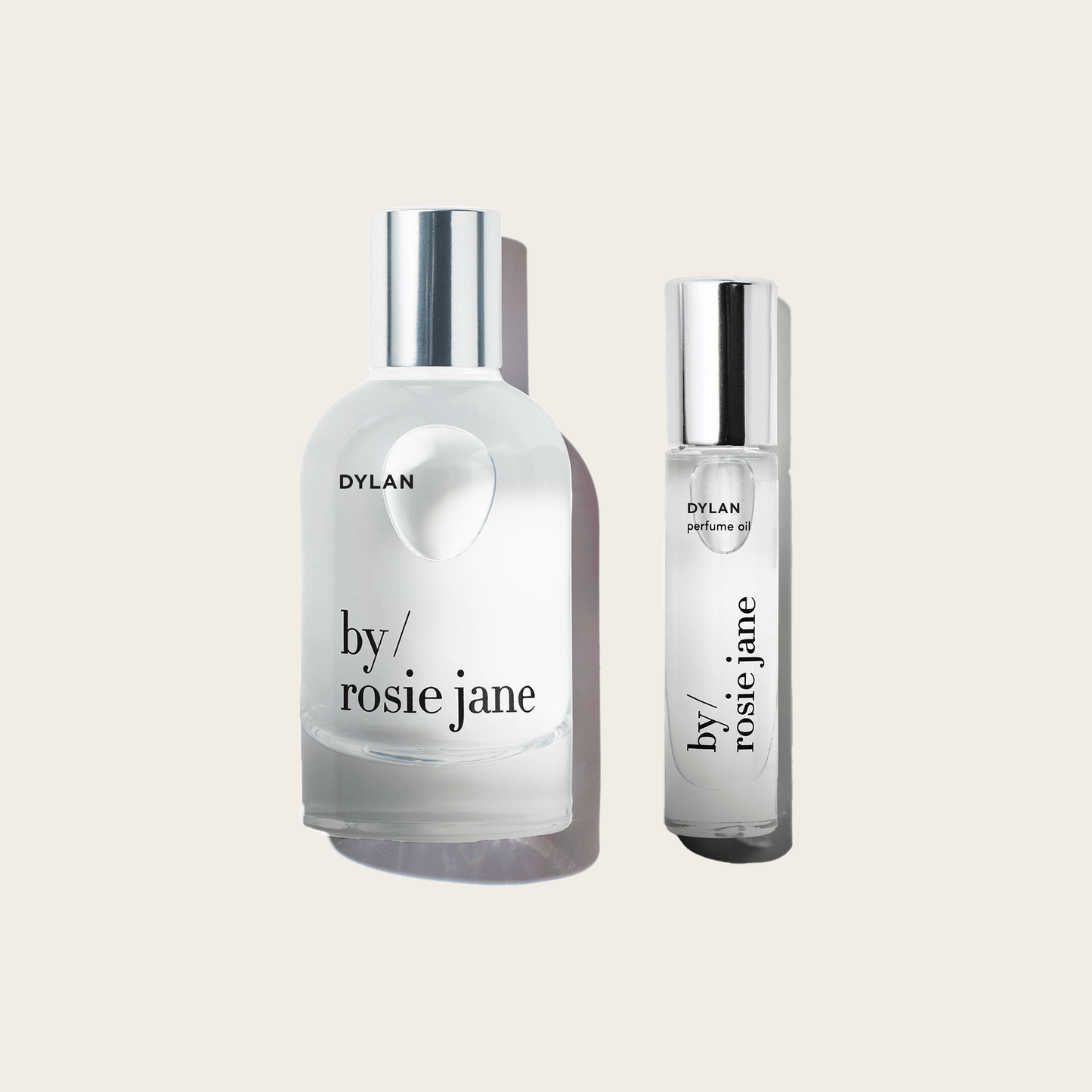 Two clear glass bottles with silver caps, labeled DYLAN byrosiejane. The DYLAN LAST ALL DAY SET features one short, round bottle and one tall, cylindrical bottle—both deliver long-lasting fragrance as Eau de Parfum or Perfume Oil. Set on a plain background.