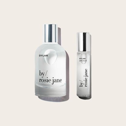 Two clear glass bottles with silver caps, labeled DYLAN byrosiejane. The DYLAN LAST ALL DAY SET features one short, round bottle and one tall, cylindrical bottle—both deliver long-lasting fragrance as Eau de Parfum or Perfume Oil. Set on a plain background.