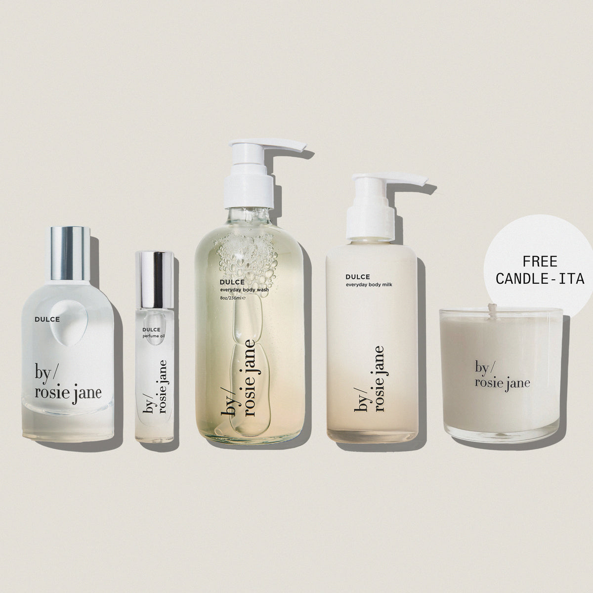 Five By Rosie Jane skincare and body care products arranged on a muted blue-gray background, including a large pump bottle, a small roller bottle, a tall body milk bottle, and a candle jar with a 'FREE CANDLE - ITA' callout. The products are mostly frosted white with clear sections and silver caps.