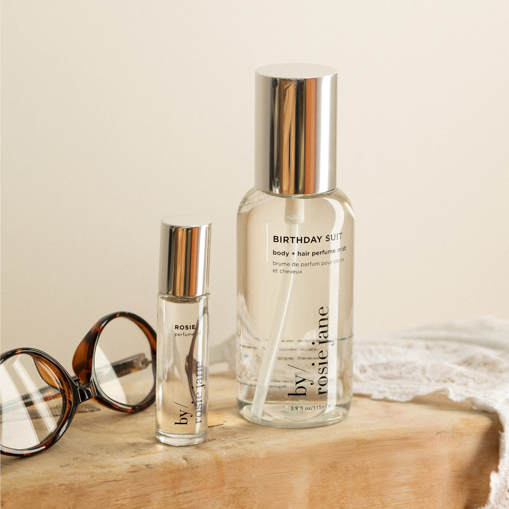 Two by rosie jane perfume bottles on a wooden surface with a neutral background