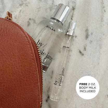 Two perfume bottles labeled 'by rosi jane' next to a brown leather pouch on a marble surface.