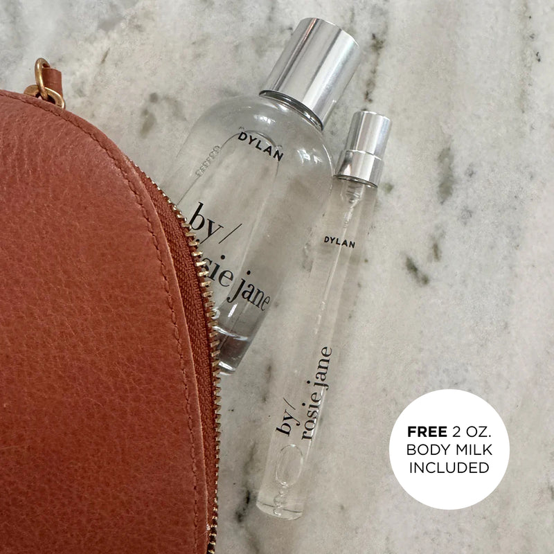 Two perfume bottles labeled 'by rosi jane' next to a brown leather pouch on a marble surface.