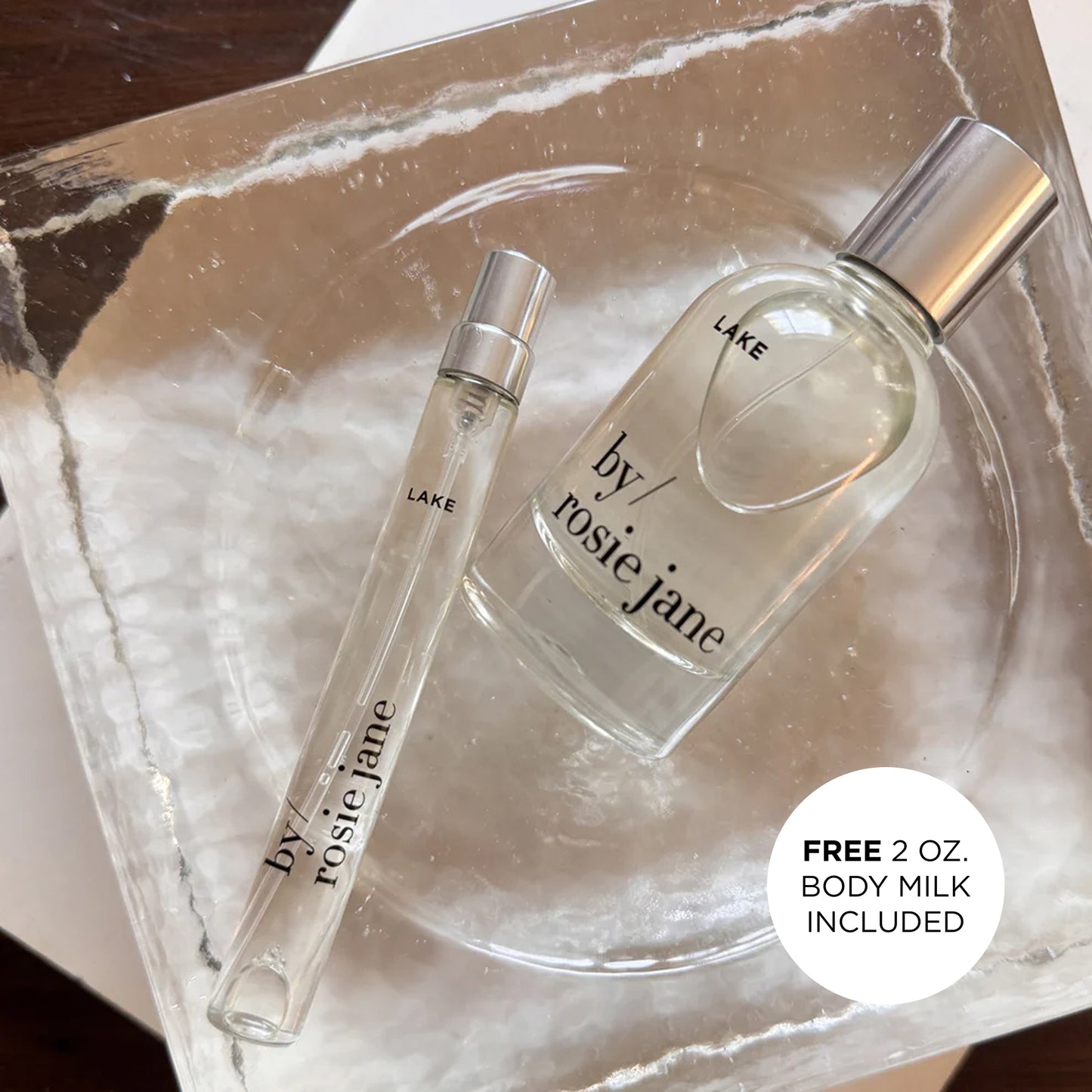Two LAKE perfume bottles by rosie jane on a marble surface with a free body milk offer.