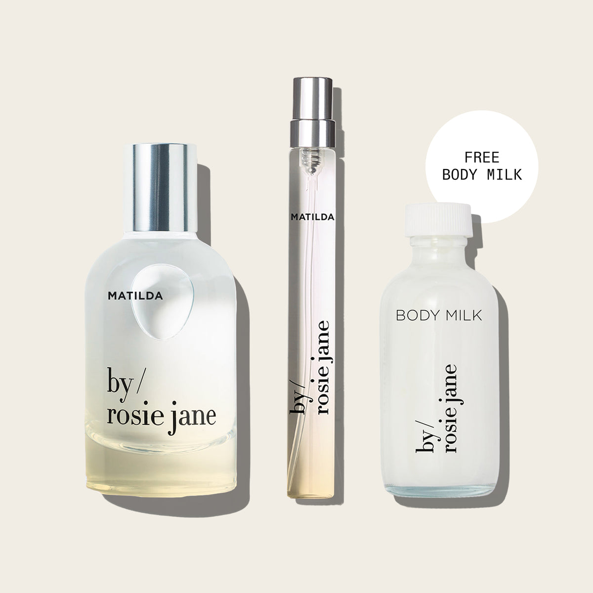 Three fragrance/body care items from by/ rosie jane arranged on a light warm beige background: a frosted bottle labeled MATILDA with a silver cap, a slim spray vial with silver cap, and a frosted bottle labeled BODY MILK. A white circular callout says FREE BODY MILK.