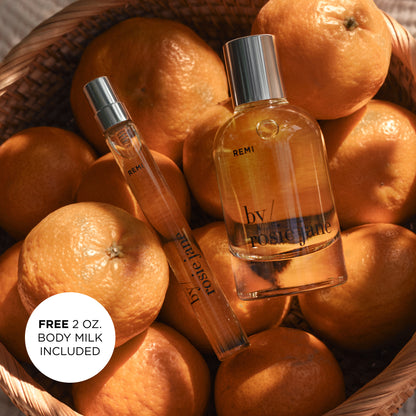Two REMI perfume bottles on a bed of oranges with a free body milk offer.