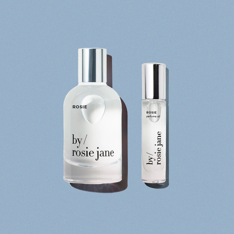 A perfume and perfume oil bottle labeled 'by rosie jane' on a light blue background