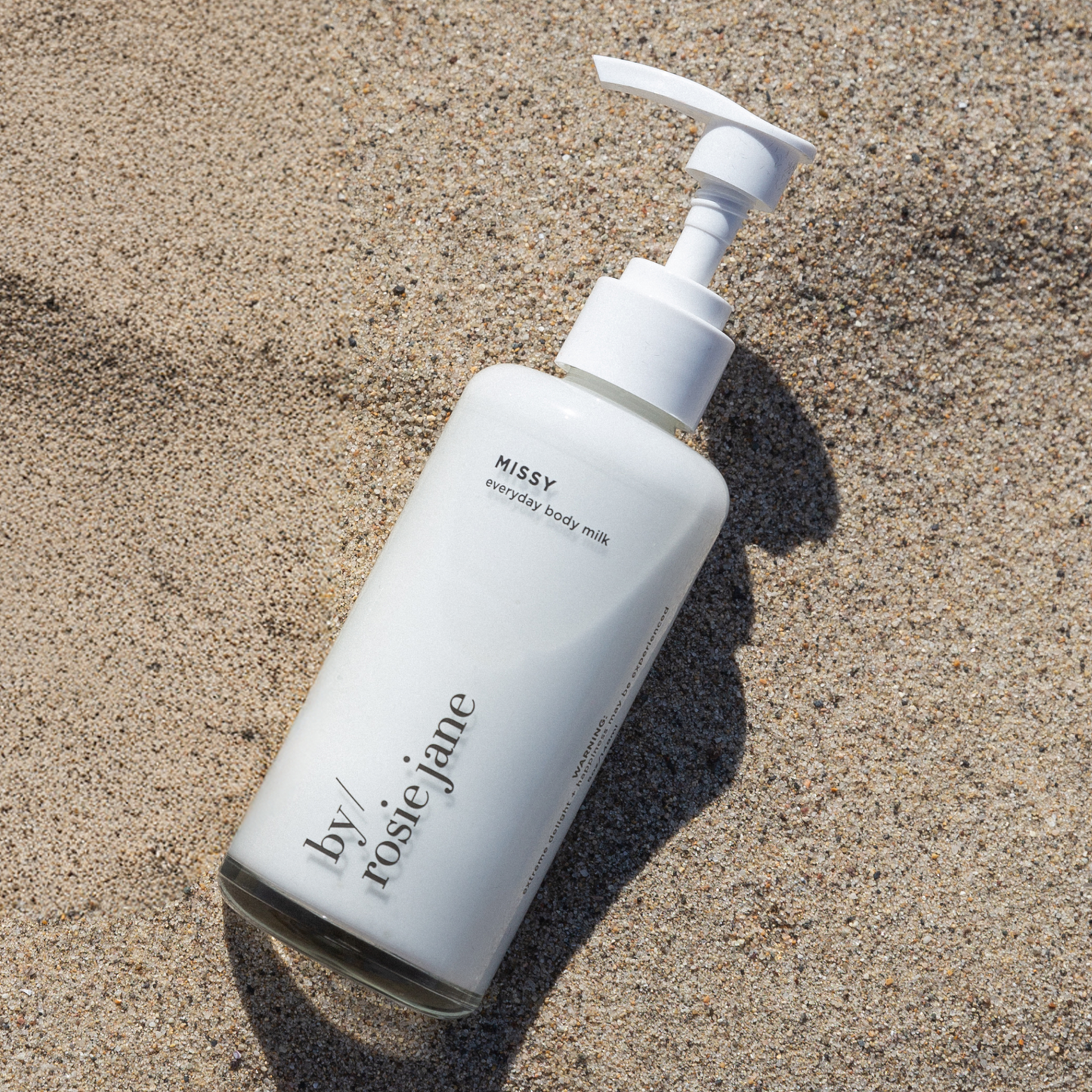 White bottle of 'by rosie jane' missy body milk on sand