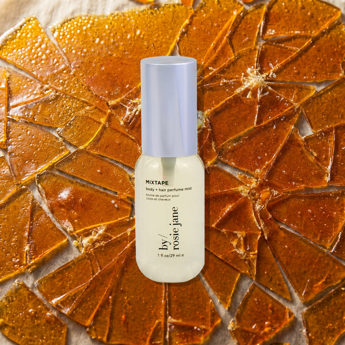 A bottle of by rosie jane body + hair mist 'MIXTAPE' stands centered against a background of broken butterscotch.