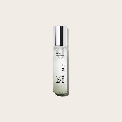 A clear glass REMI PERFUME OIL bottle by byrosiejane with a silver cap, photographed against a plain light beige background.