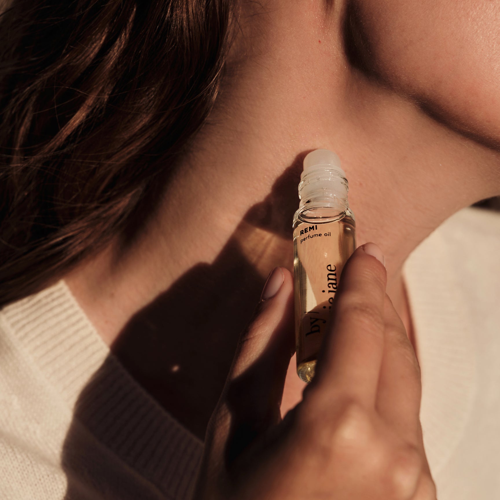 woman holding a REMI perfume bottle near their neck