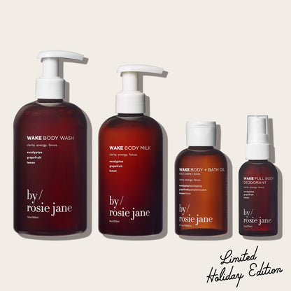 Set of 'by rosie jane' wake skincare products including body wash, milk, oil, and deodorant on a beige background.