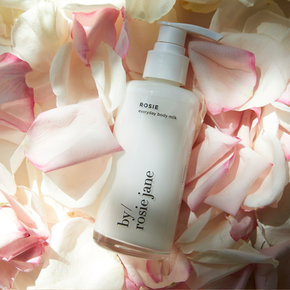 Bottle of 'by rosie jane' body milk on a bed of pink and white rose petals