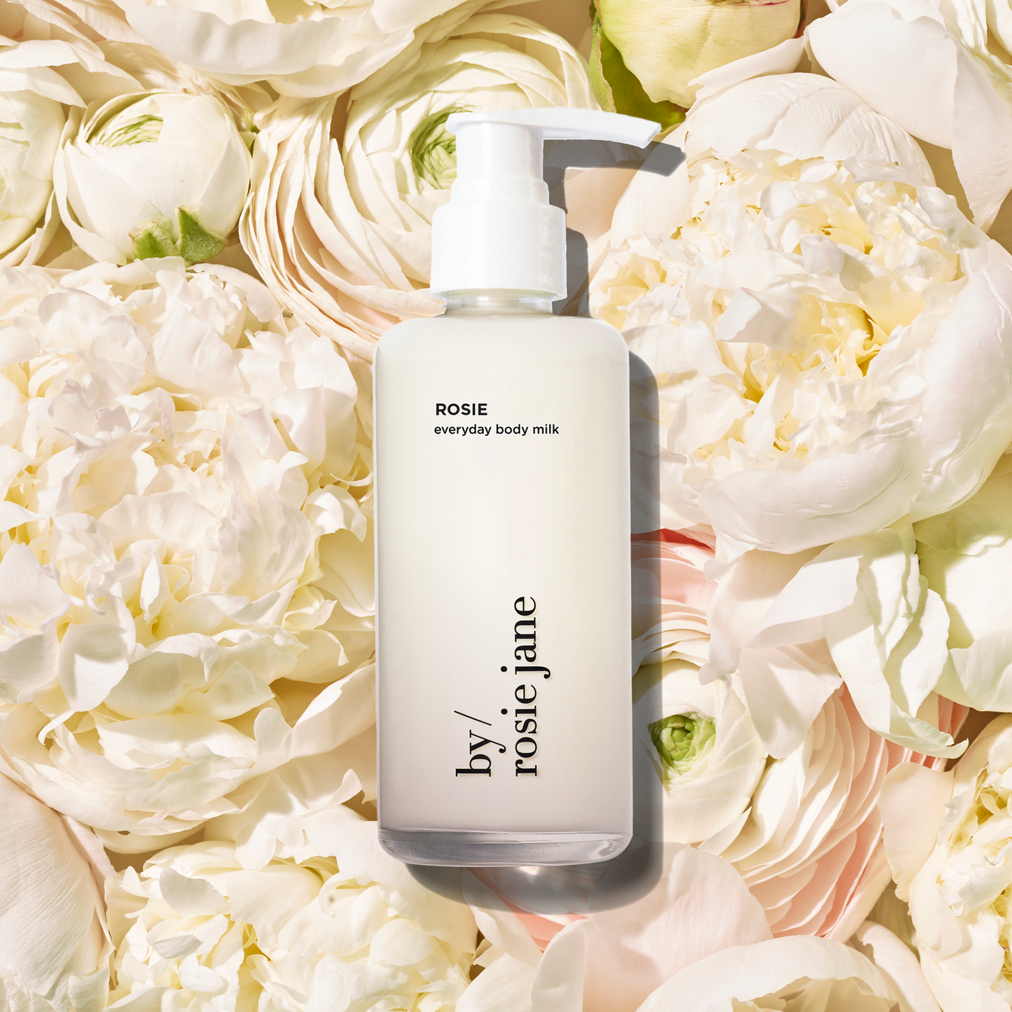 Body milk bottle labeled 'by rosie jane' on a bed of white flowers