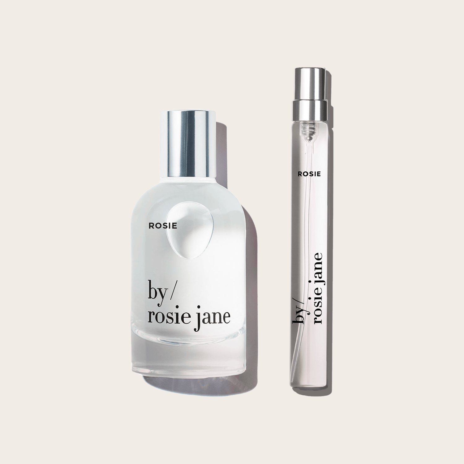 A clear glass HOME + AWAY SET eau de parfum bottle with a silver cap by byrosiejane sits beside a slim perfume spray, both part of a limited edition set, on a light beige background.