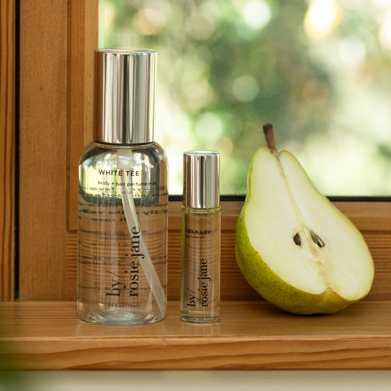 Two bottles of 'by rosie jane' skincare products on a wooden surface with a pear.
