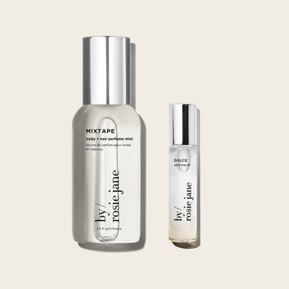 Two clear cosmetic bottles with silver caps on a light warm gray background: a larger bottle labeled MIXTAPE body + hair perfume mist and a smaller bottle labeled DULCE perfume oil, both from by rosie jane.