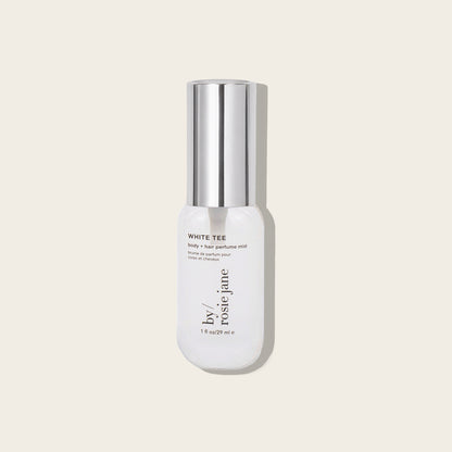 A bottle of by Rosie Jane White Tee Fortify + Hair Perfume Mist, featuring a white bottle and a reflective silver cap, set against a solid light beige background.