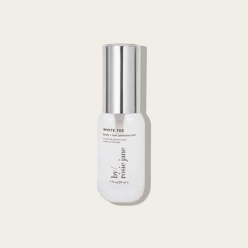 A bottle of by Rosie Jane White Tee Fortify + Hair Perfume Mist, featuring a white bottle and a reflective silver cap, set against a solid light beige background.