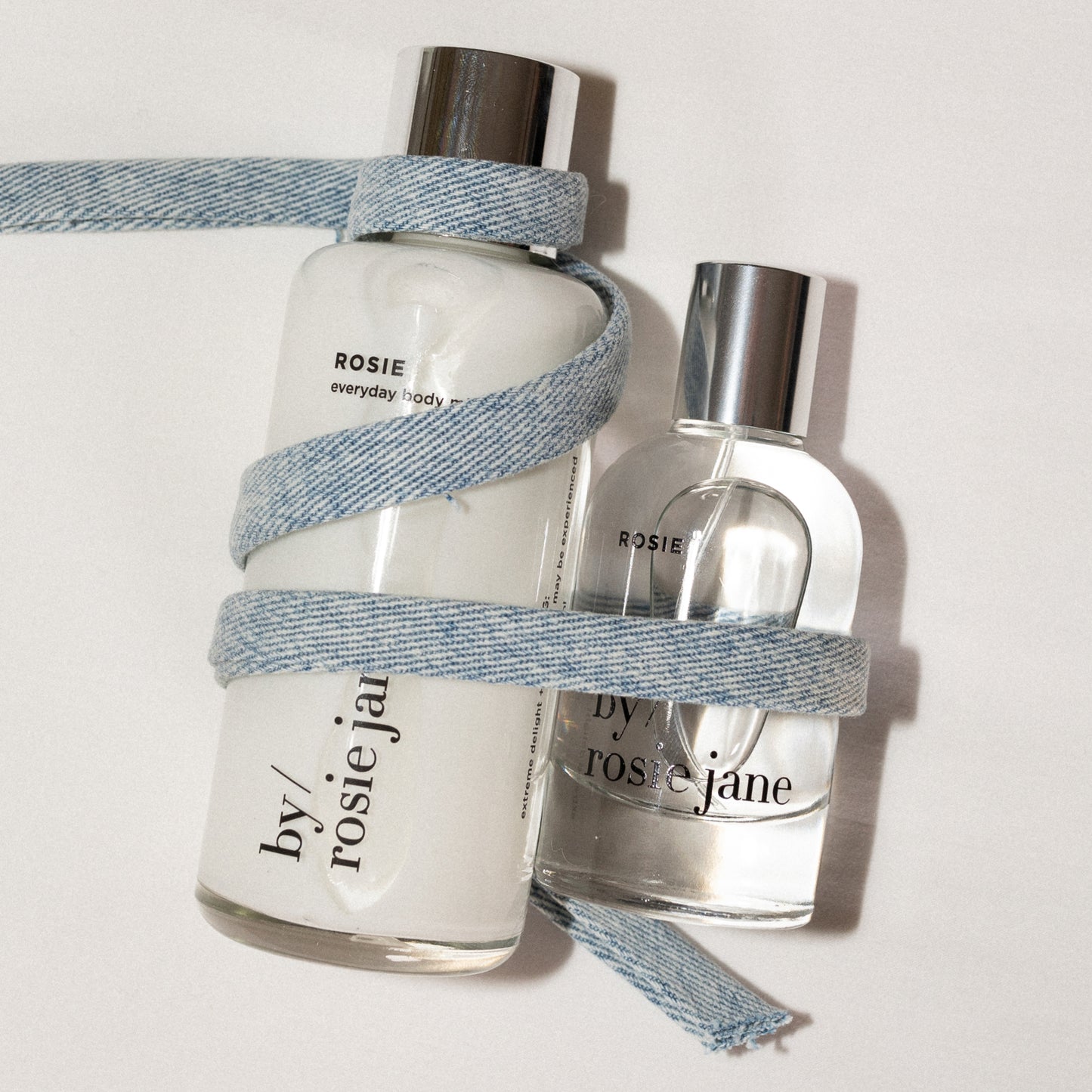 Two bottles by Rosie Jane with denim straps on a light background- body milk and perfume