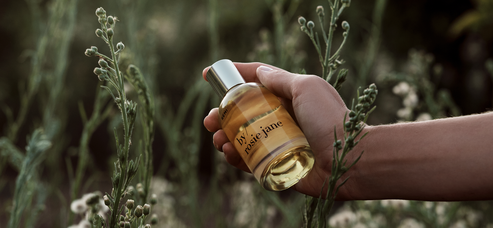 hand holding a bottle of remi perfume in a field of greenery